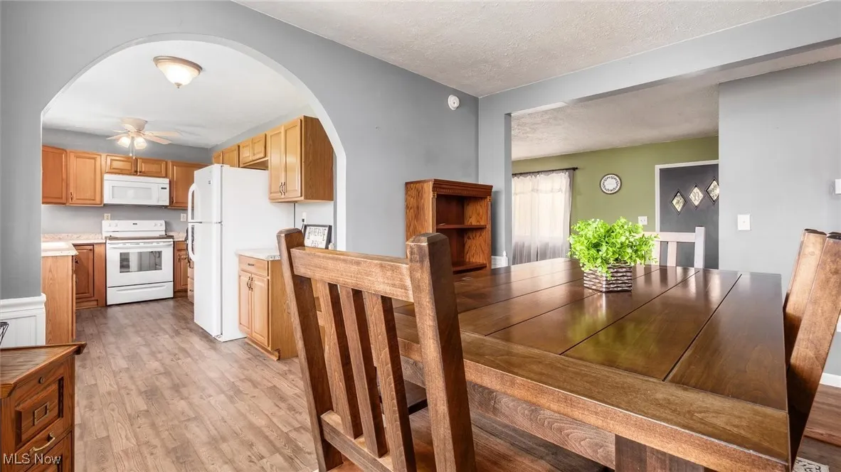 Dining room featuring arched walkways, light wood finished floors, a ceiling fan, and a textured ceiling