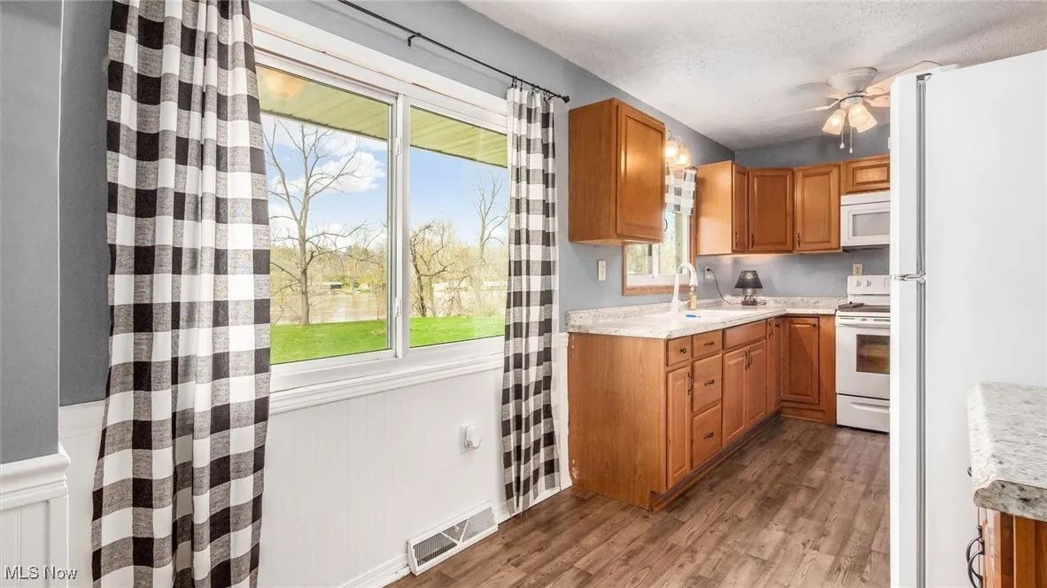 Kitchen with ceiling fan, white appliances, visible vents, wood finished floors, and a sink