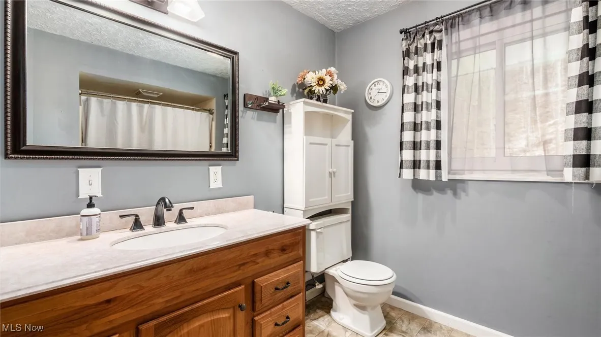 Bathroom with toilet, a textured ceiling, vanity, and baseboards