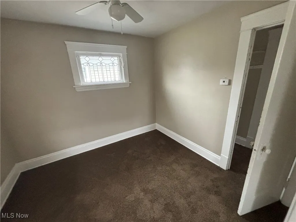 Spare room with dark carpet, baseboards, and a ceiling fan