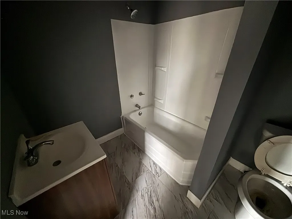 Full bathroom with shower / bathtub combination, toilet, marble finish floor, a sink, and baseboards