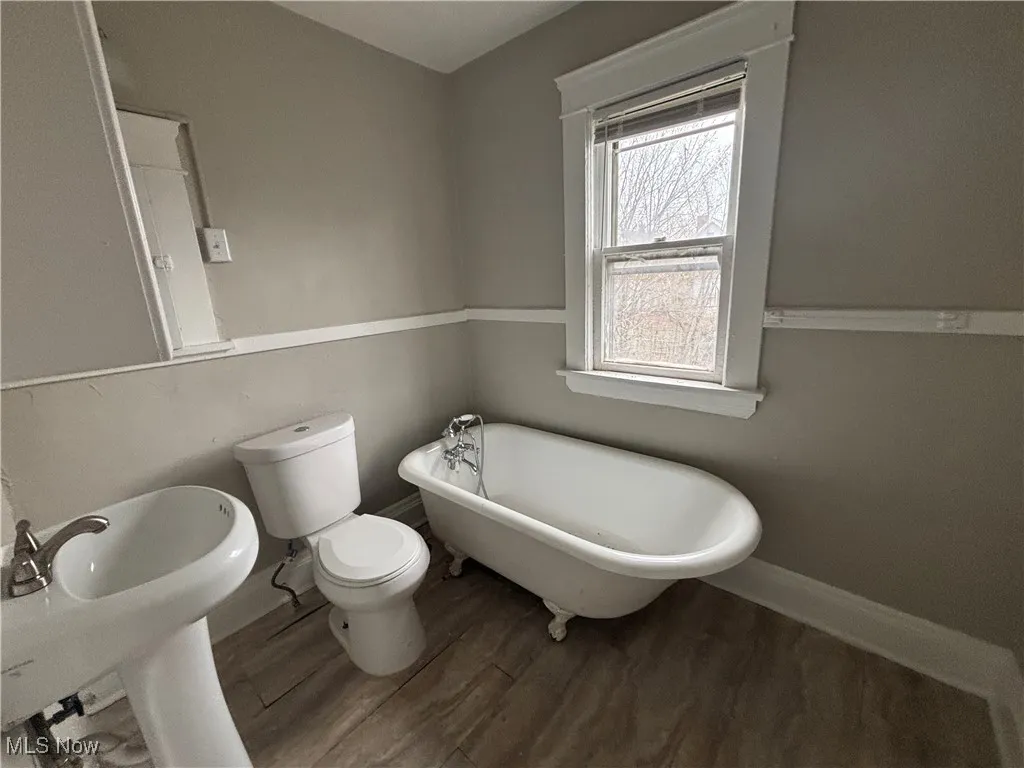 Full bathroom featuring toilet, a freestanding tub, wood finished floors, and baseboards