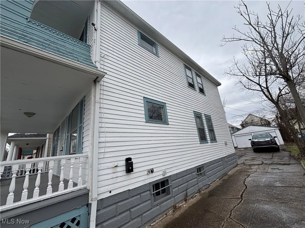 View of side of property with a porch, an outdoor structure, and driveway
