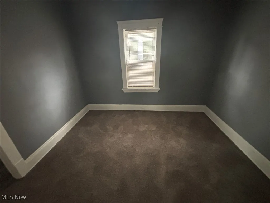 Spare room with baseboards and dark colored carpet