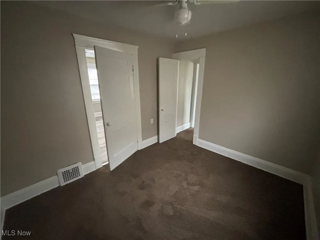Unfurnished bedroom featuring visible vents, baseboards, dark carpet, and a ceiling fan