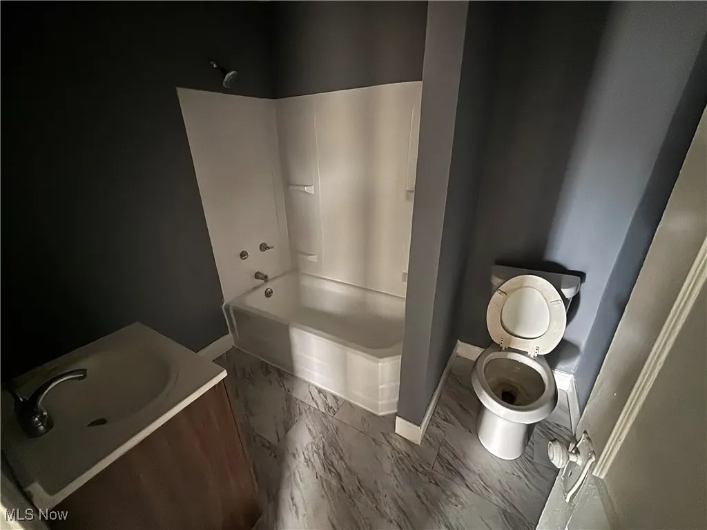 Bathroom featuring toilet, marble finish floor, shower / tub combination, and baseboards