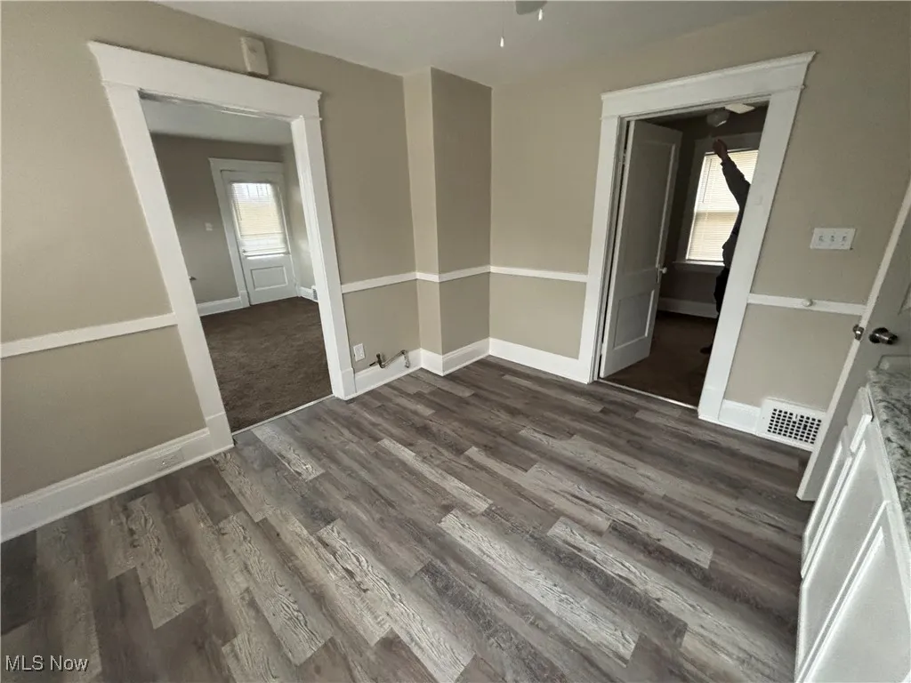 Empty room with dark wood-type flooring, visible vents, and baseboards