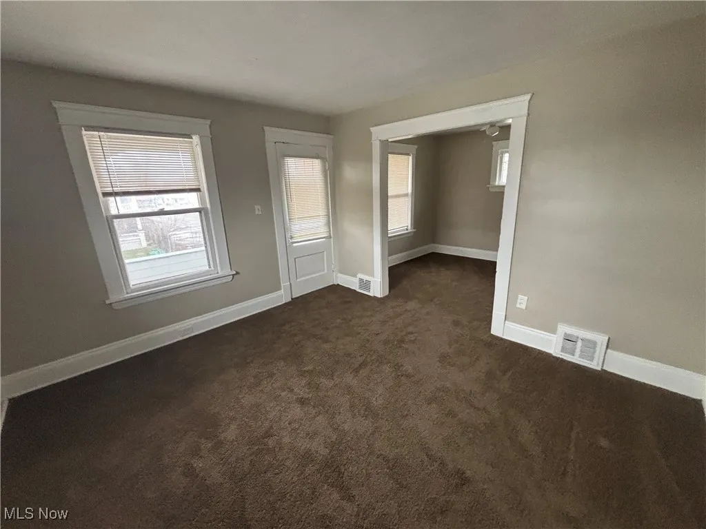 Empty room featuring dark colored carpet, visible vents, and baseboards
