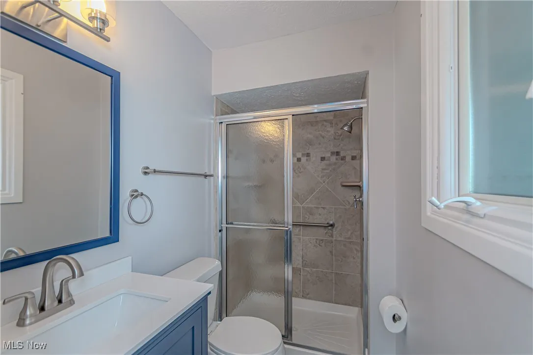 Bathroom featuring toilet, a stall shower, vanity, and a textured ceiling
