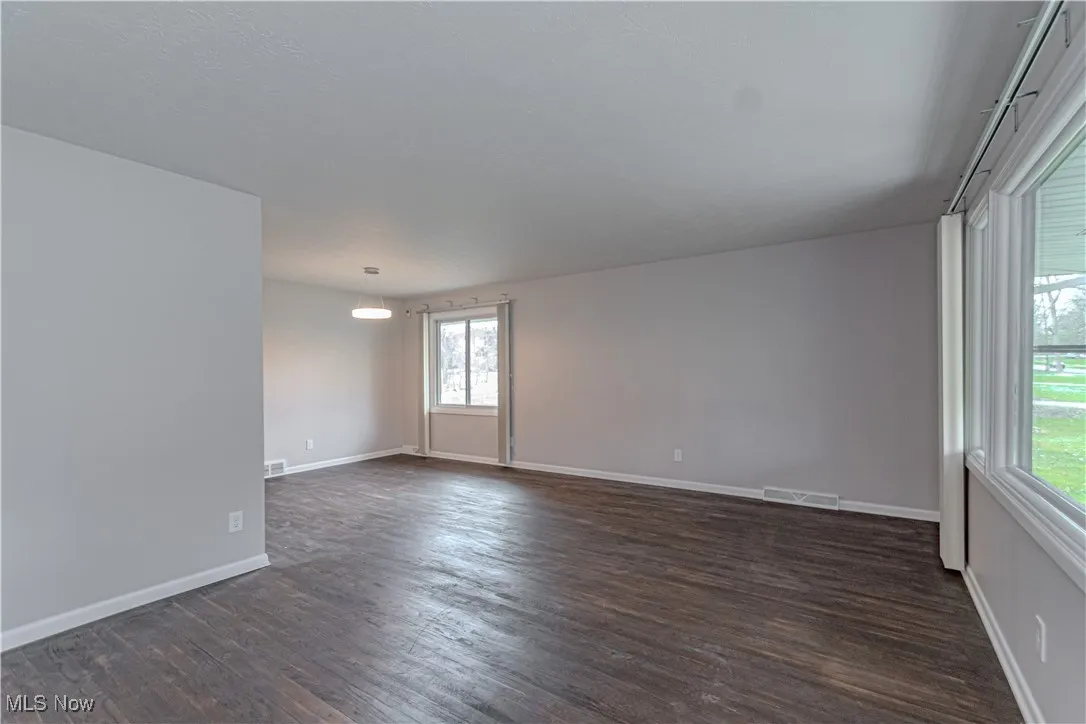 Unfurnished room featuring dark wood-style flooring, baseboards, and visible vents