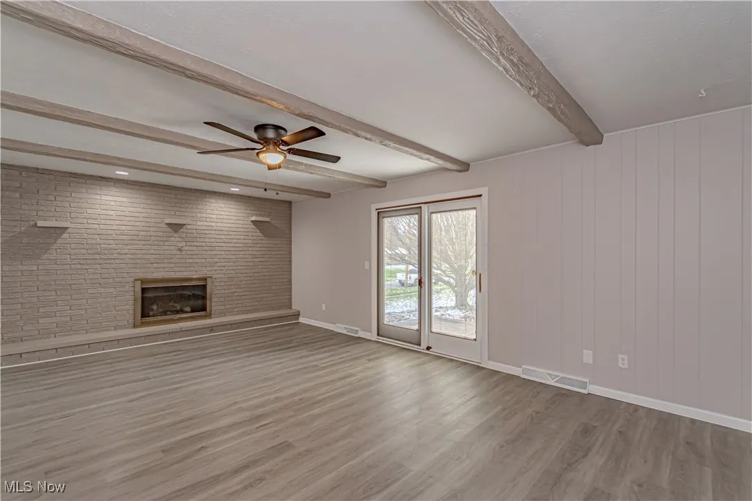 Unfurnished living room featuring visible vents, ceiling fan, a fireplace, beamed ceiling, and wood finished floors