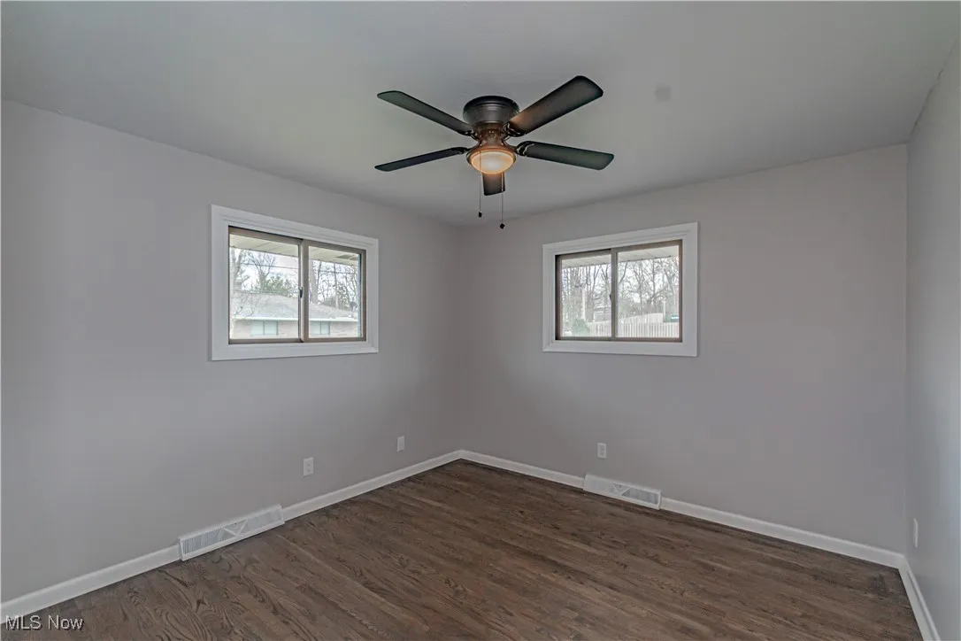 Unfurnished room featuring ceiling fan, visible vents, baseboards, and dark wood finished floors
