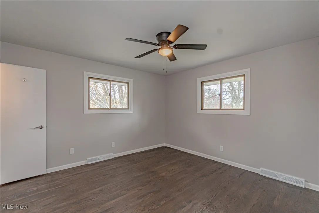 Unfurnished room featuring dark wood-type flooring, visible vents, and a wealth of natural light