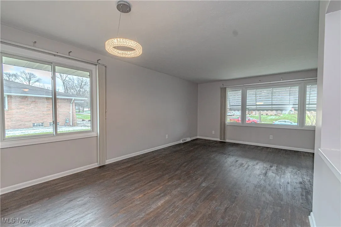 Empty room with plenty of natural light, dark wood-type flooring, and baseboards