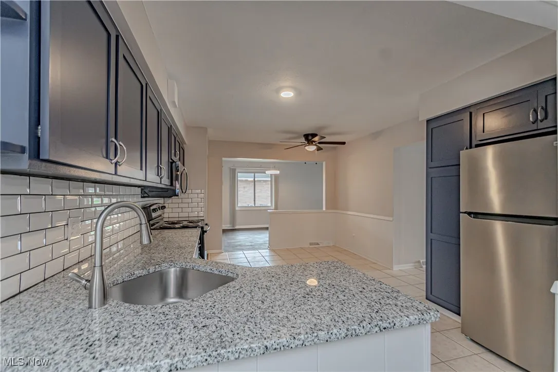 Kitchen featuring light tile patterned floors, a ceiling fan, a sink, stainless steel appliances, and backsplash