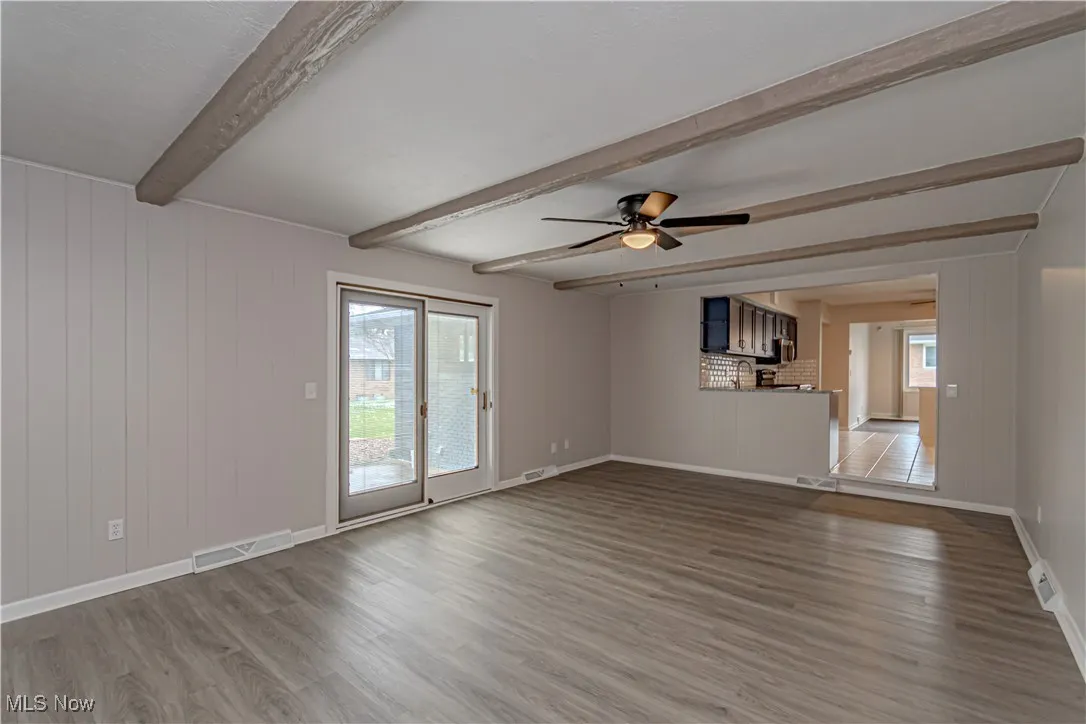 Empty room with baseboards, a ceiling fan, visible vents, beamed ceiling, and wood finished floors