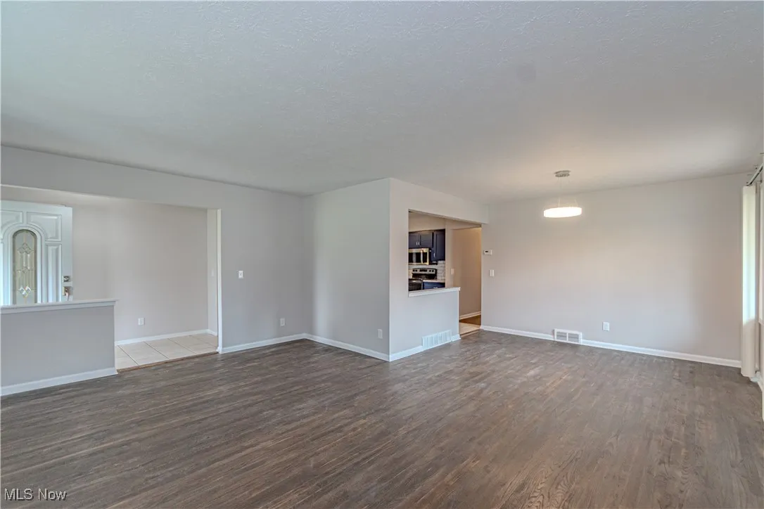 Unfurnished living room featuring visible vents, baseboards, a textured ceiling, and dark wood finished floors