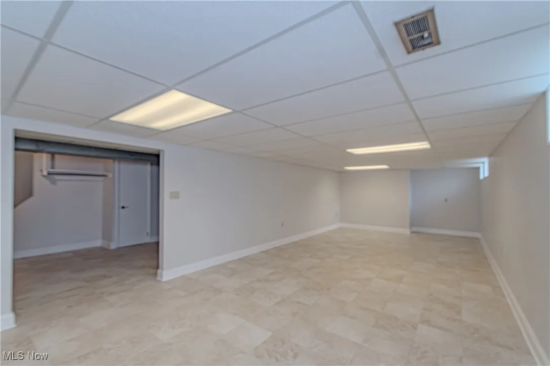 Finished below grade area featuring visible vents, baseboards, and a paneled ceiling