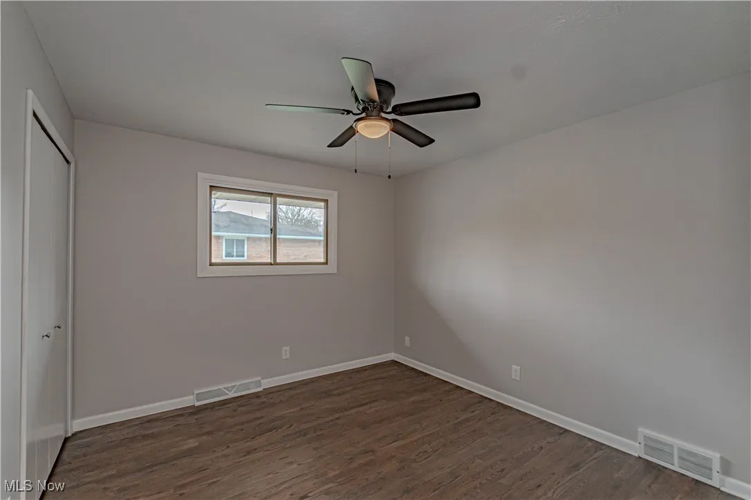 Unfurnished bedroom with dark wood-style flooring, visible vents, baseboards, and a closet
