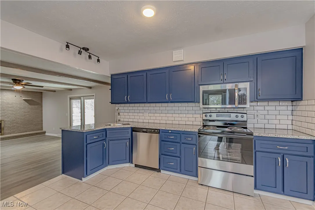 Kitchen with appliances with stainless steel finishes, blue cabinetry, light tile patterned flooring, and a peninsula
