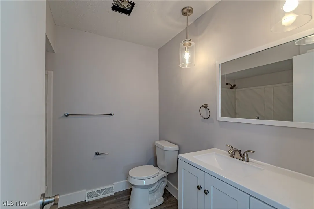 Full bathroom with vanity, visible vents, toilet, wood finished floors, and baseboards