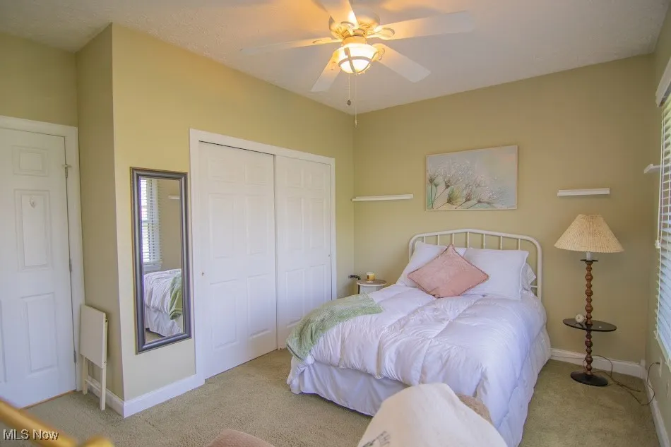 Carpeted bedroom with a closet, baseboards, and a ceiling fan