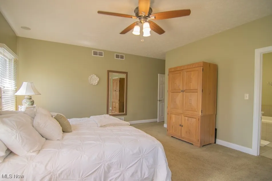 Bedroom featuring light carpet, baseboards, visible vents, and ensuite bath