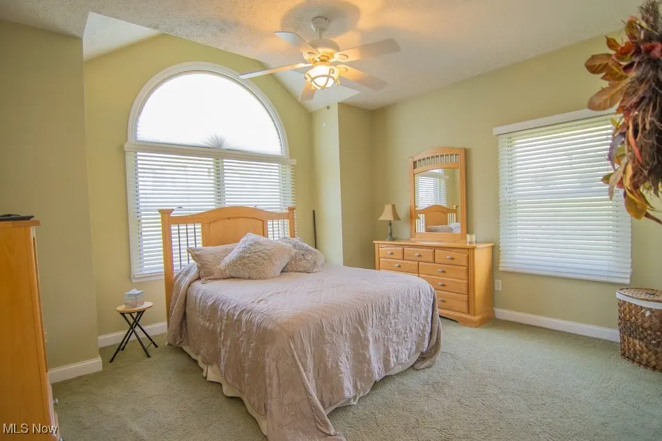Bedroom with baseboards, a ceiling fan, a textured ceiling, light carpet, and lofted ceiling