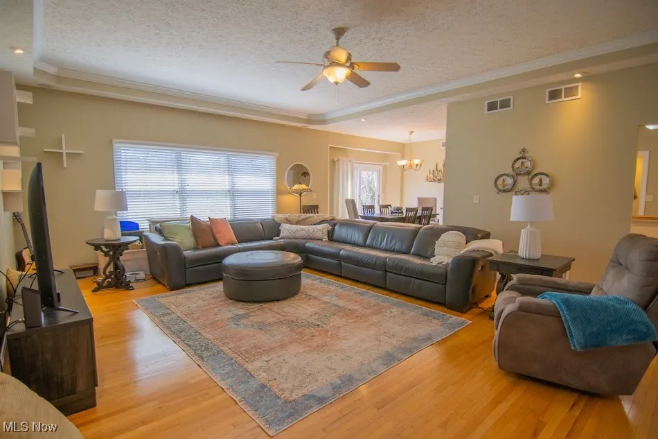 Living area with light wood-type flooring, ceiling fan with notable chandelier, and a textured ceiling
