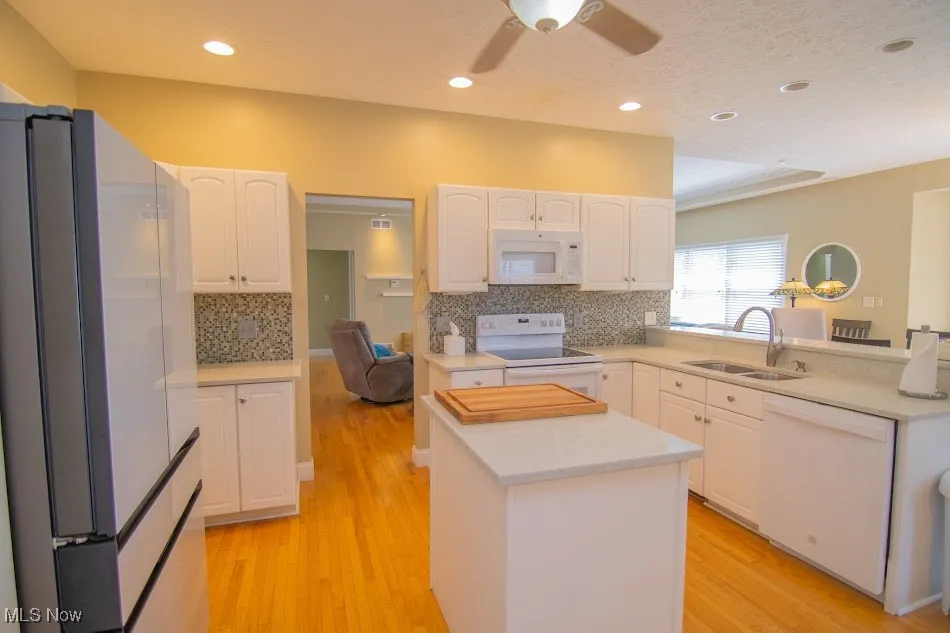 Kitchen featuring white cabinets, a sink, light countertops, white appliances, and light wood-style floors