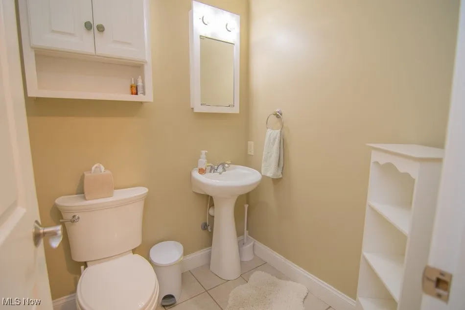 Half bathroom with toilet, tile patterned floors, and baseboards
