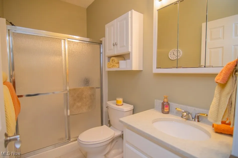 Bathroom with toilet, vanity, and a stall shower