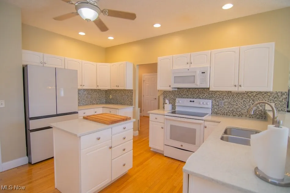 Kitchen featuring a sink, white cabinets, and white appliances