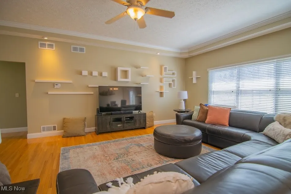 Living area featuring a textured ceiling, wood finished floors, ceiling fan, and visible vents
