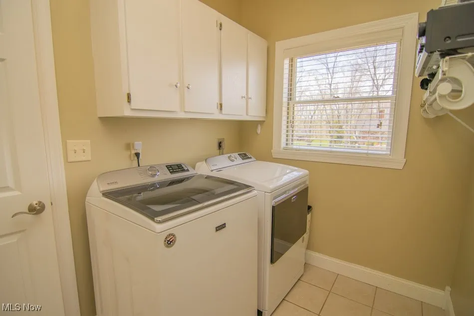 Laundry room with light tile patterned floors, baseboards, cabinet space, and washer and clothes dryer