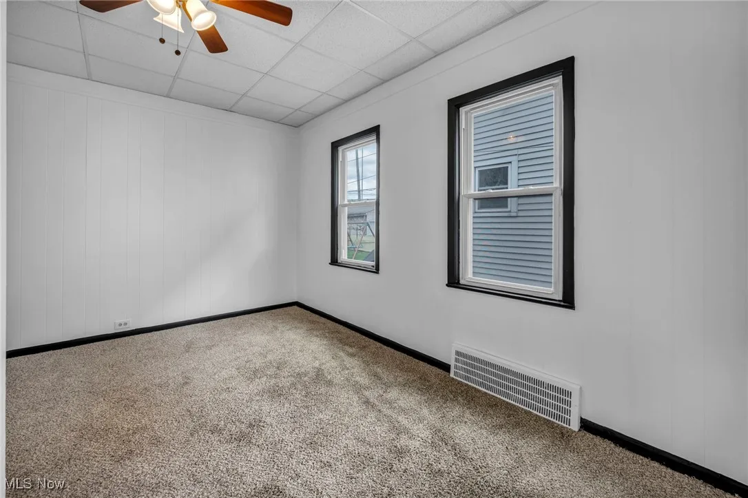 Carpeted spare room featuring visible vents, ceiling fan, a drop ceiling, and baseboards