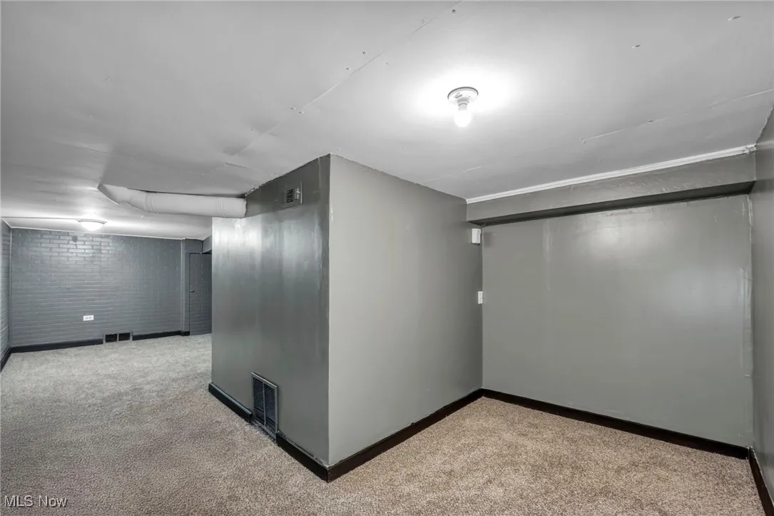 Finished below grade area featuring brick wall, carpet flooring, and visible vents