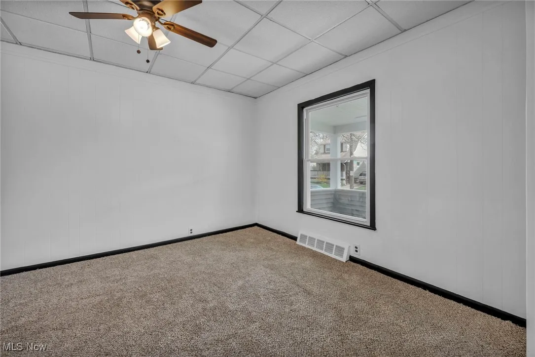 Carpeted empty room featuring visible vents, ceiling fan, a paneled ceiling, and baseboards