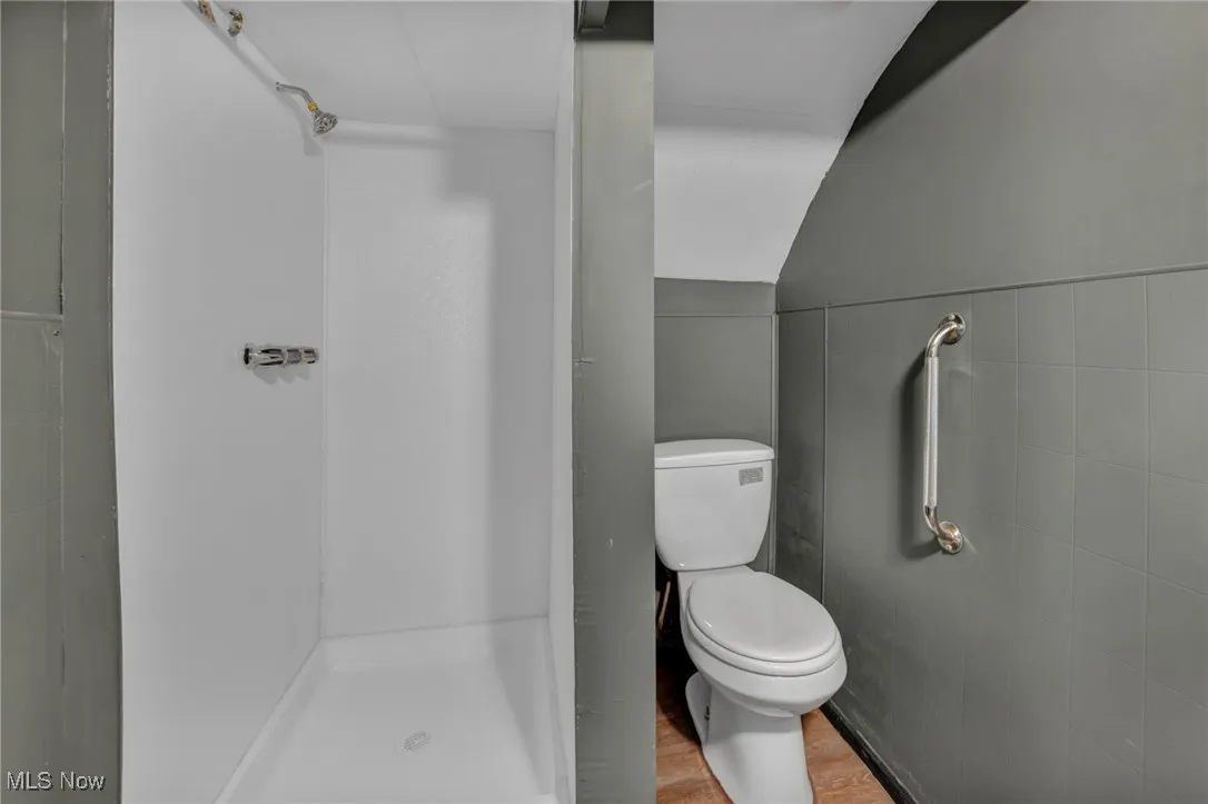 Full bath with vaulted ceiling, a stall shower, toilet, tile walls, and wood finished floors