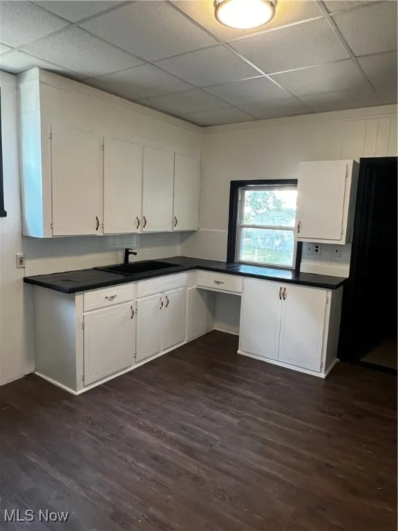 Kitchen with a drop ceiling, dark wood finished floors, white cabinets, dark countertops, and built in desk