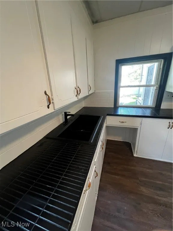 Kitchen with tile counters, built in desk, white cabinets, dark wood-type flooring, and backsplash