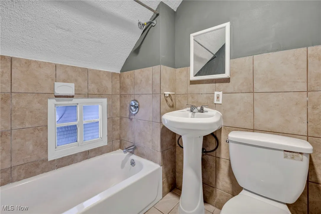 Bathroom with a textured ceiling, tile walls, and toilet
