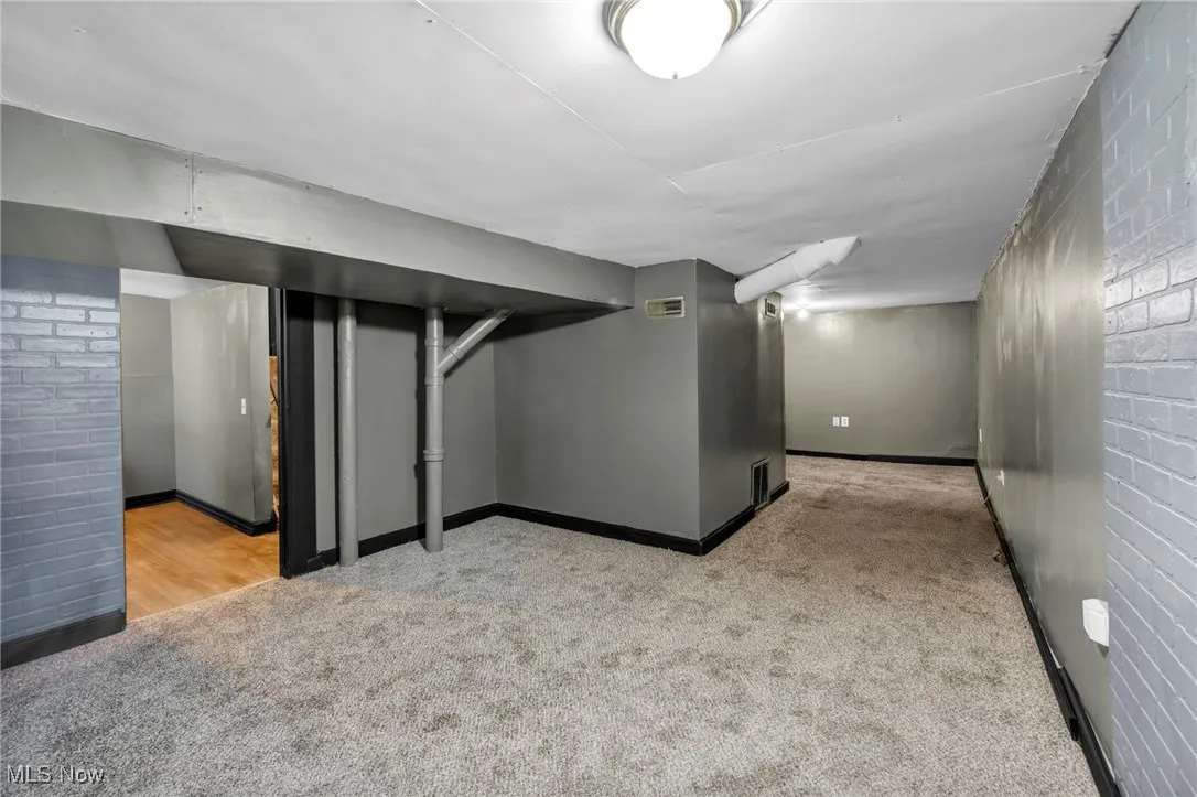 Finished below grade area with carpet floors, brick wall, and visible vents