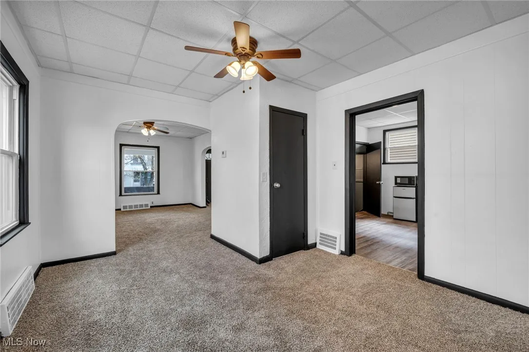 Empty room featuring arched walkways, carpet, visible vents, and a ceiling fan