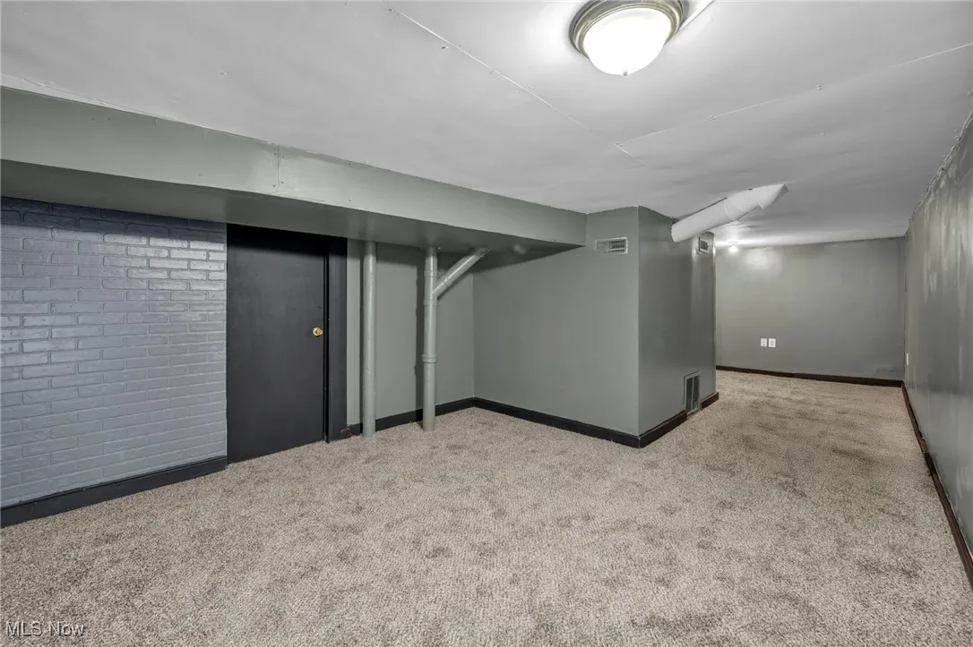 Finished below grade area featuring brick wall, baseboards, visible vents, and carpet floors