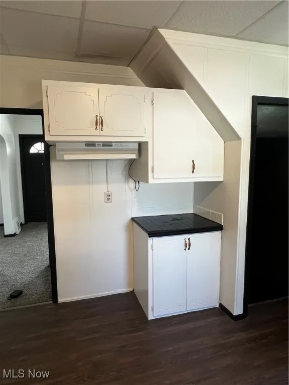 Kitchen featuring range hood, dark wood-type flooring, white cabinets, and dark countertops