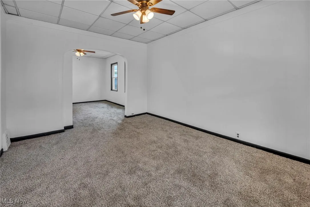 Carpeted spare room featuring arched walkways, a paneled ceiling, baseboards, and ceiling fan