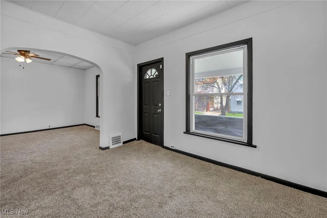 Entrance foyer with baseboards, a ceiling fan, carpet floors, visible vents, and arched walkways