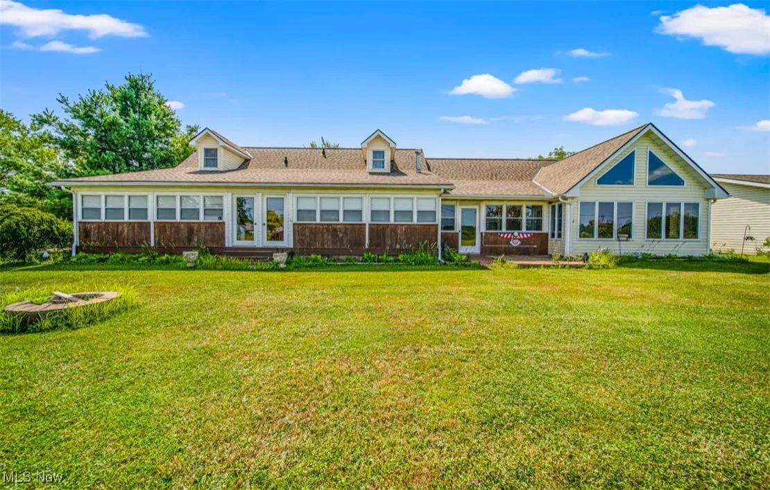 Rear view of house featuring a lawn, a fire pit, and a shingled roof