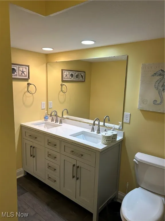 Bathroom featuring a sink, toilet, double vanity, and wood finished floors
